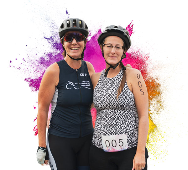 Two Women wearing bike helmets smiling for camera with colourful paint splash behind them